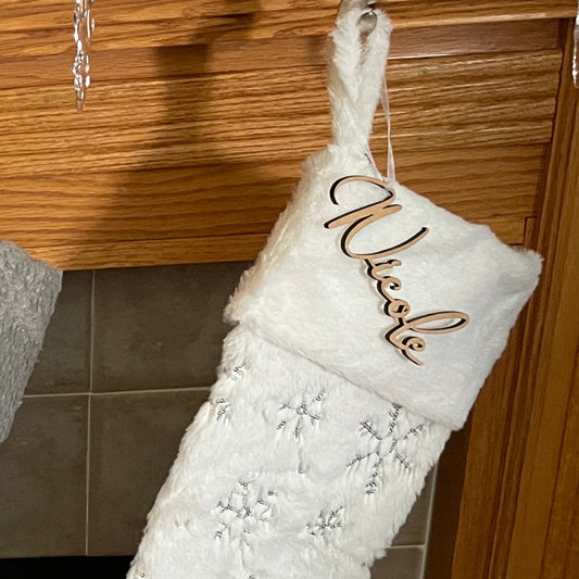 Stocking tag “nicole” on a white snowflake stocking over a mantle.