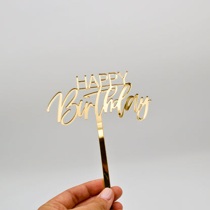 Gold mirrored acrylic cake topper. “happy”is in bold thin letters. “Birthday” is in a cursive font.