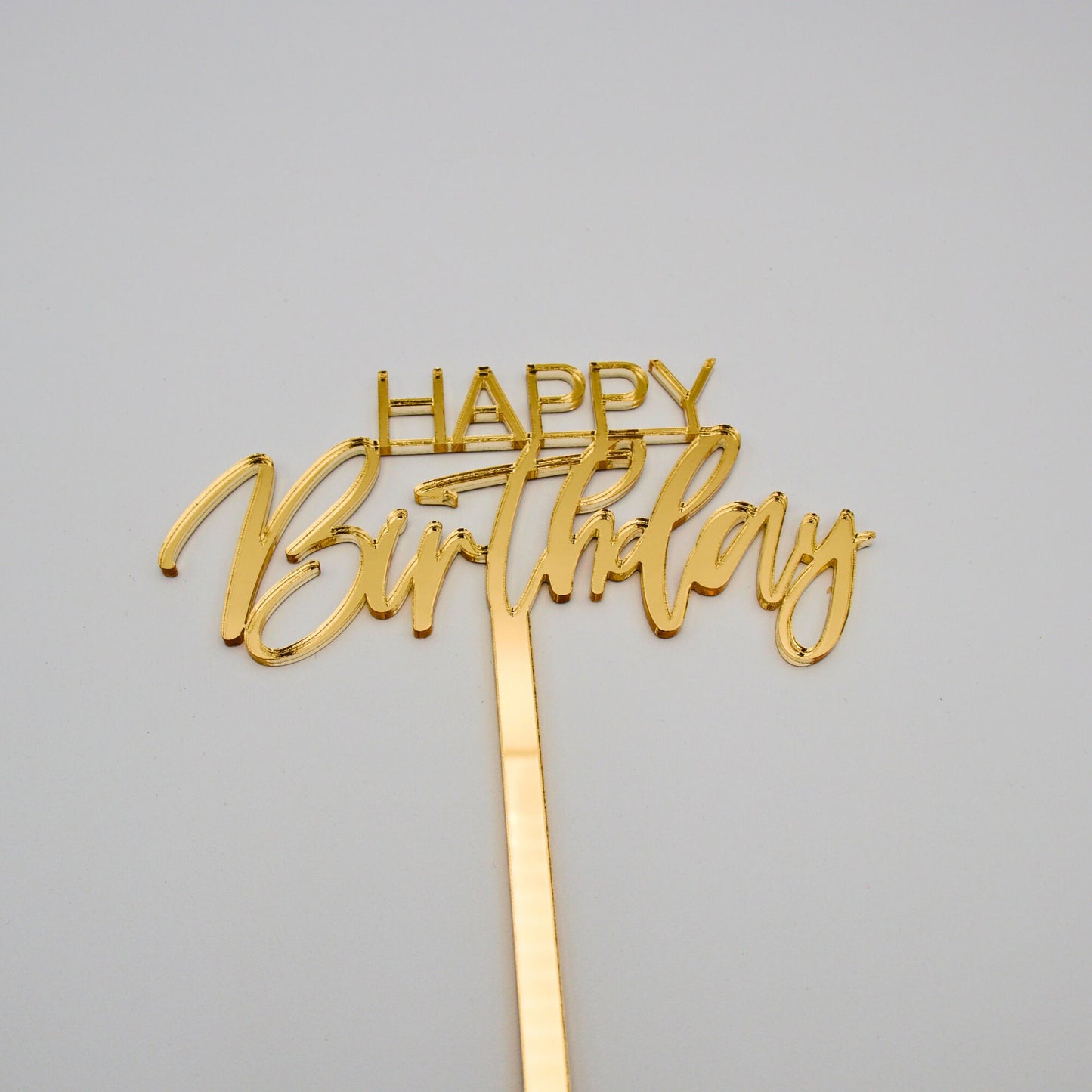 Gold mirrored acrylic cake topper. “happy”is in bold thin letters. “Birthday” is in a cursive font.