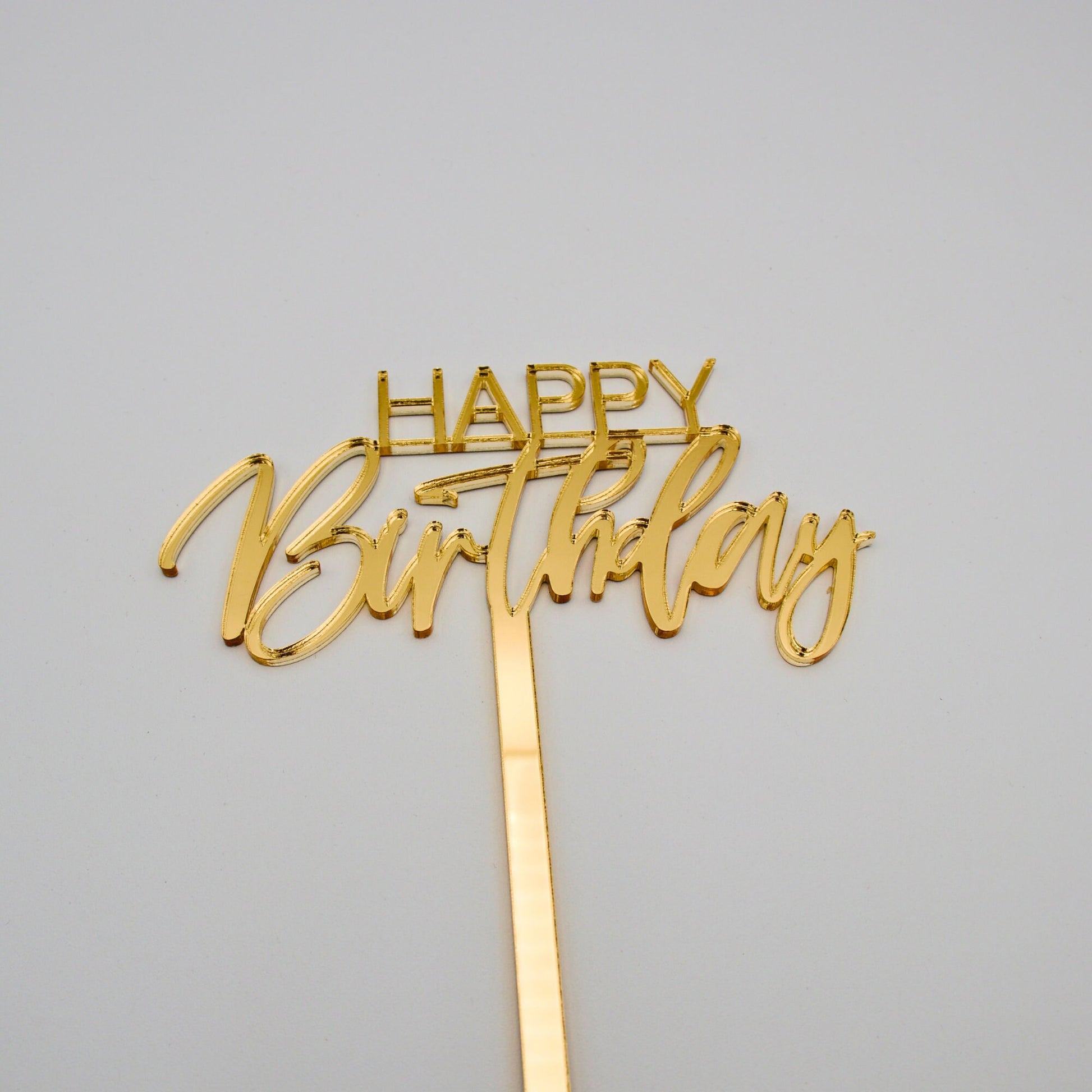 Gold mirrored acrylic cake topper. “happy”is in bold thin letters. “Birthday” is in a cursive font.