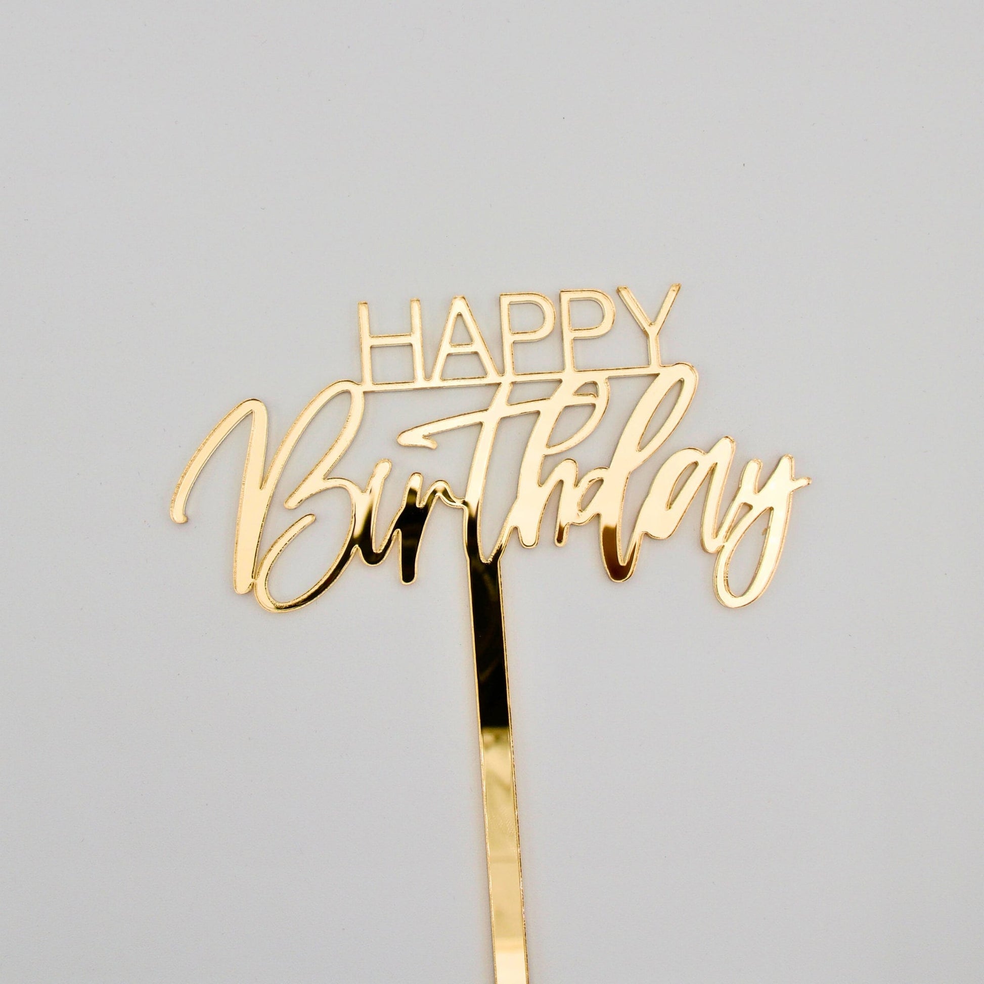 Close up of Gold mirrored acrylic cake topper. “happy”is in bold thin letters. “Birthday” is in a cursive font.